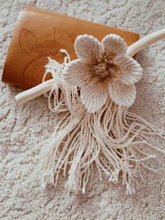 a crocheted flower on the floor next to a leather book and knitting needles