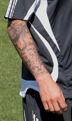 a man with tattoos on his arm standing in front of a soccer ball and grass field