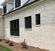 a brick house with three windows and two bushes in front of the window sill