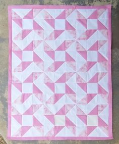 a pink and white quilt is laying on the ground with it's diagonal design