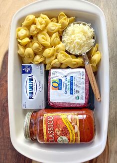 a white bowl filled with pasta, sauce and other food items on top of a wooden table