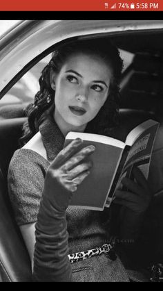 a woman sitting in the back seat of a car holding a book and looking at the camera