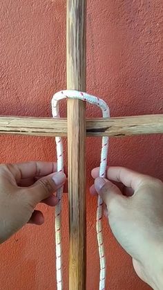 two hands are making a cross out of wood and rope with white paint on it