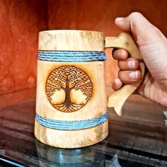 a hand holding a wooden mug with a tree on the front and blue rope around it