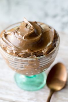 a glass bowl filled with chocolate frosting next to two spoons on a table