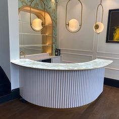 a curved counter in the middle of a room with mirrors on the wall and lights hanging above it