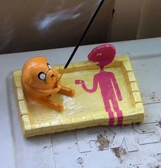 a yellow tray with an orange and pink figure in it on top of a table