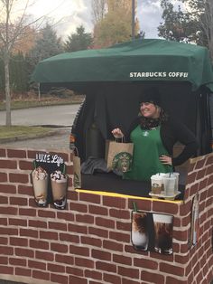 a woman standing behind a brick wall holding starbucks bags