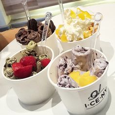 three cups filled with different types of ice cream and strawberries on top of a table