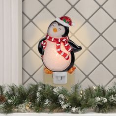 a light up penguin with a red hat and scarf on it's head sitting on a mantle