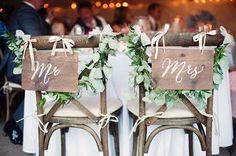 two wooden chairs decorated with greenery and mr and mrs signs are sitting side by side