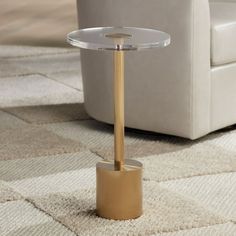 a glass table with a gold base on a carpeted floor next to a white chair