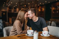 a man and woman sitting at a table with two coffee cups in front of them