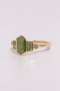 Art deco inspired ring featuring Jade and August's birthstone, peridot. The glowing green centerstone is British Columbia Jade, and it has beautiful depth of color. The jade is inlaid into the elongated hexagon, measuring 9.5mm x 5mm. Light green Arizona peridot are at the sides, and are approximately .30 total carat worth. Millimeter measurement from end to end is 15mm. Your choice of gold color and karat. Band is 1.75mm thick. Please leave a note at checkout with your preferred size. All gems Art Deco Green Jewelry With Accent Stones, Art Deco Green Ring With Bezel Setting, Art Deco Green Emerald Multi-stone Ring, Green Art Deco Jewelry With Accent Stones, Art Deco Green Emerald Ring In 14k Gold, Art Deco Emerald Ring In 14k Gold, Art Deco Green Jewelry With Bezel Setting, Green Art Deco Jewelry With Bezel Setting, Green Octagon Ring With Bezel Setting