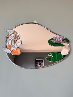 a mirror with an image of a fish and flowers on the bottom is hanging on a wall