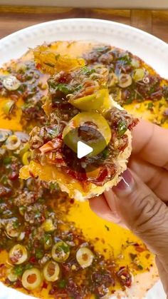 someone is holding up a piece of food on top of a plate with olives