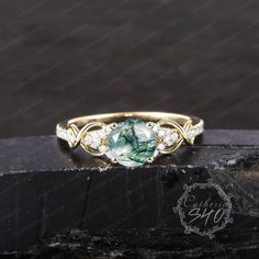 a gold ring with green and white stones on the side, sitting on top of a black