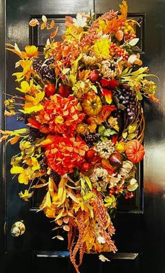 a wreath is hanging on the door with autumn flowers and leaves around it in front of a black door