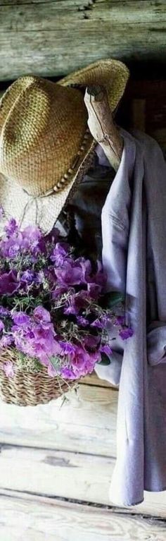 purple flowers are in a basket next to a hat and coat on a wooden bench