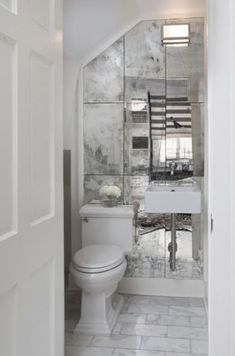 a white toilet sitting under a bathroom mirror next to a sink and toilet paper dispenser