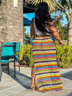 a woman is walking down the sidewalk wearing a multicolored crochet skirt