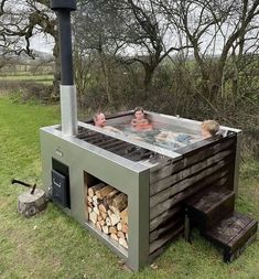 two people sitting in an outdoor hot tub with firewood stacked on the side and one person standing next to it