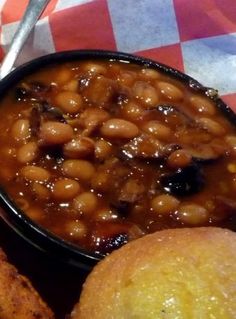 baked beans in a black bowl next to some bread on a checkered table cloth