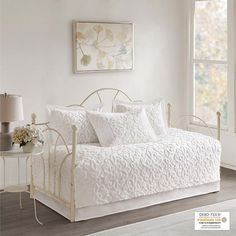 a white daybed in a bedroom next to a window and table with flowers on it