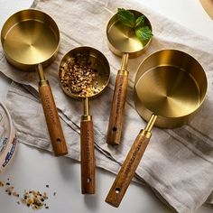 four brass measuring spoons with wooden handles on a linen napkin next to some spices