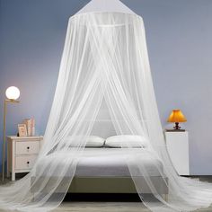 a bed with a white canopy over it in a room next to a dresser and lamp