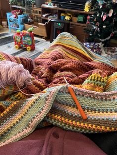 a crocheted blanket is laying on the floor next to a ball of yarn