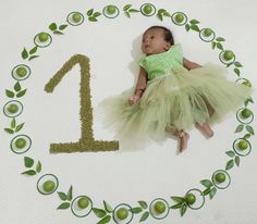 a baby in a green dress laying on the floor next to a number one sign