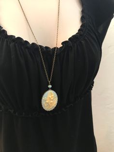 "Here is a beautiful blue lily of the valley cameo necklace. This is a large cameo which features nicely detailed lily of the valley flowers against a dreamy blue background. This cameo is set in an oxidized brass setting and is suspended from one Czech glass bead along with a high quality long brass chain. All materials are lead and nickel safe, cameo is resin. Handcrafted in the USA by Botanical Bird. This necklace comes shipped in a lovely gift box. Cameo Pendant measures: 1 1/4\" across x 1 Blue Oval Locket Necklace, Oval Blue Locket Necklace, Victorian Blue Cameo Jewelry, Blue Victorian Jewelry With Vintage Charm, Blue Cameo Jewelry For Wedding, Blue Cameo Necklace For Wedding, Vintage Birth Flower Pendant Jewelry, Vintage Birth Flower Necklaces For Jewelry Making, Elegant Blue Jewelry With Birth Flower