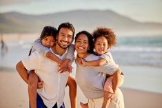 three adults and two children are hugging on the beach