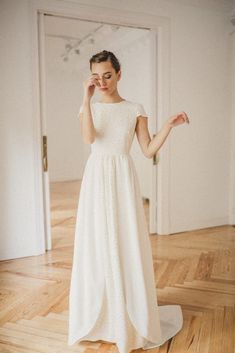 a woman in a white dress standing on a hard wood floor with her hands behind her head