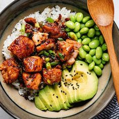 a bowl filled with chicken, rice and vegetables next to a wooden spoon on top of a table