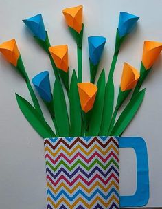 there are paper flowers in a vase with green stems and orange tulips sticking out of it