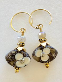 "Beautiful artisan lampwork bead earrings with hand painted white flower motif in light brown, amber, and white accented with leafy gold bead caps on 24k gold vermeil ear wires. The gorgeous translucent lampwork beads are 12 x 18 x 7mm ovals with smooth matte finish and raised floral design. Slivers of glass and fine silver are used to \"draw\" the intricate designs then beads are kiln fired at +900 degrees. The result is a unique one of a kind lampwork bead. Lovely flower beads are topped with Glass Flower Earrings, Lampwork Bead Earrings, Lampwork Earring, Aquamarine Earrings, Flower Motif, Flower Beads, Handmade Copper, Beaded Necklaces, Sterling Silver Hoops