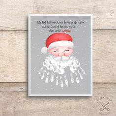 a christmas card with a santa claus face and snow falling down the middle, on top of a wooden surface