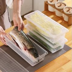 a woman preparing food on top of a cutting board next to plastic containers filled with vegetables and fish