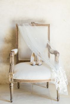 the bride's wedding shoes are sitting on an antique chair with a veil draped over it