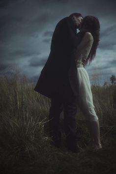 a man and woman kissing in front of a dark sky with the moon behind them