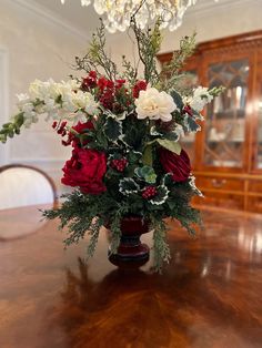 a vase filled with red and white flowers on top of a wooden table next to a chandelier