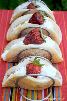 a row of hot dogs covered in frosting and strawberries sitting on top of a table