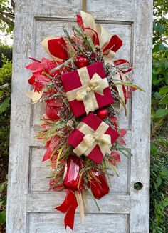 a wreath with red and gold bows hanging on a white door frame in front of some bushes