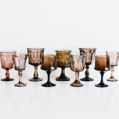 an assortment of wine goblets are lined up in a row on a white surface