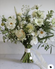 a bouquet of white flowers in a vase with a ribbon tied around the bottom half