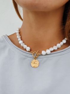 'Lucie' - a modern take on a classic pearl necklace. Beautiful freshwater baroque pearls combined with a gold toggle clasp and a 24k gold plated 925 sterling silver coin pendant. Pearls are symbolic of wisdom gained through experience. The gems are believed to offer protection, as well as attract good luck and wealth. Pearls are symbolic of the wearer's loyalty, generosity, integrity, and purity The surface of the pearls may have few bumps and ridges that indicate the natural origin of the pearls. The necklace is approximately 42 cm in length, lenght varies slightly due to natural size differences in pearls. Wear it alone or layered with other necklaces from our collection: https://www.etsy.com/shop/hippieplumedesigns?section_id=14540137&ref=shopsection_leftnav_2 How to take care of your j Pearl Necklace With Gold, Gold Coin Pendant, Jewelry Necklace Simple, Ancient Greek Jewelry, Gold Medallion Necklace, Pearl Necklace Choker, Classic Pearl Necklace, Greek Jewelry, Freshwater Pearl Necklace