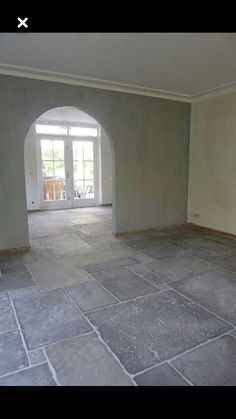 an empty living room with stone flooring and arched doorway leading to the patio area