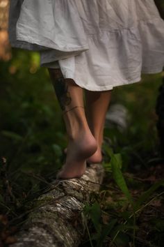 a woman with tattoos walking on a log in the woods